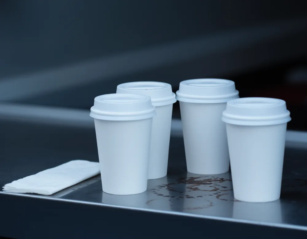White paper cups with lids standing on the scuffed steel counter ledge of the hatch